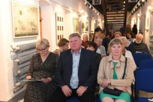 Widownia koncertu. W pierwszym rządzie siedzą dwie kobiety i mężczyzna