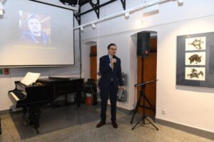 Piotr Romańczyk, młody mężczyzna w garniturze przemawia. W rękach ma mikrofon. Za nim znajduje się ekran, na którym wyświetla się zdjęcie młodego mężczyzny i napis "pamięci Tomasza Świergosza (1986-2022)"