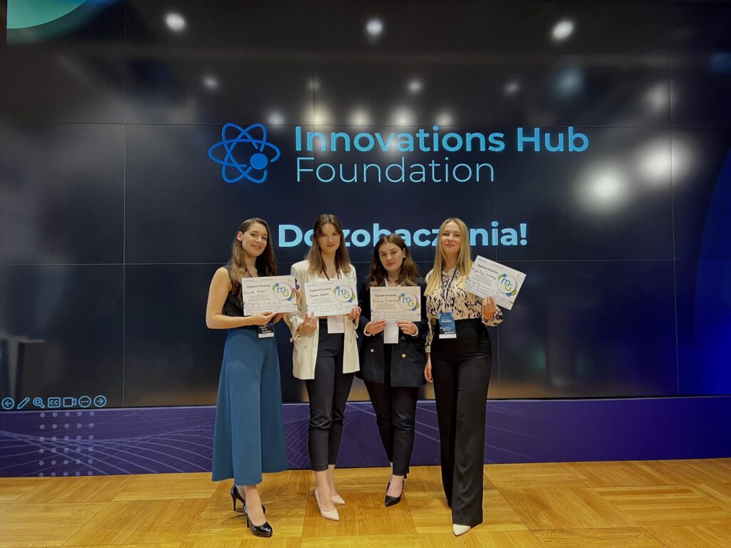 Cztery dziewczyny stoją na scenie. W rękach trzymają dyplomy. Są elegancko ubrane. Za nimi wyświetla się napis Innovations Hub Foundation; Do zobaczenia!