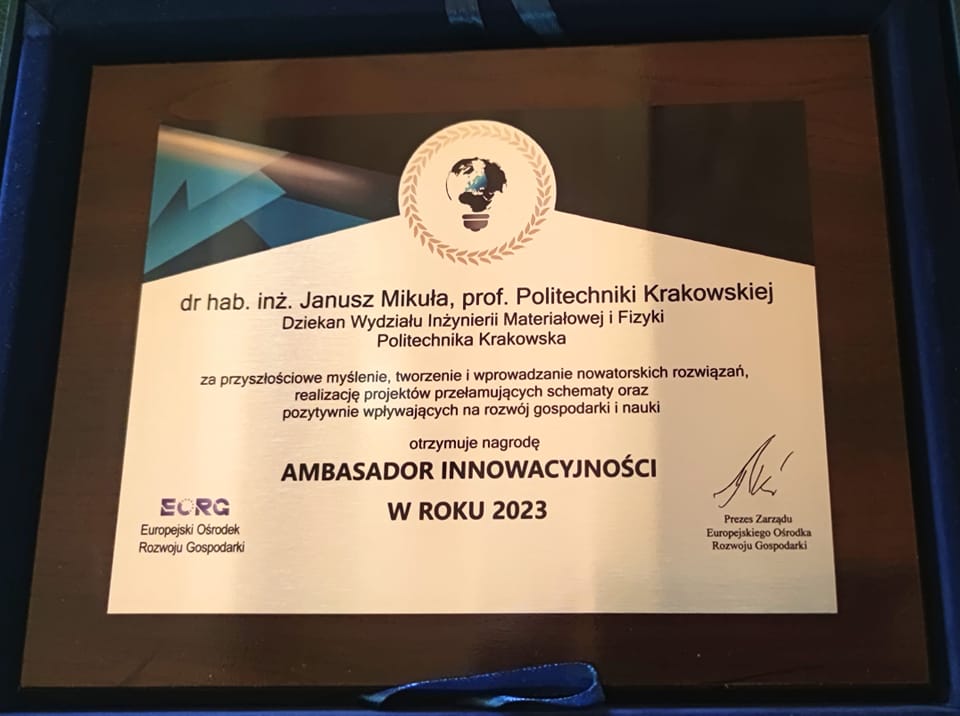 Granatowe pudełko. W nim w brązowej ramce nagroda-dyplom. U góry na środku grafika przedstawiająca żarówkę, w której umieszczona jest kula ziemska, a całość otoczona wieńcem laurowym. Poniżej napis: dr hab. inż. Janusz Mikuła, prof. Politechniki Krakowskiej Dziekan Wydziału Inżynierii Materiałowej i Fizyki Politechnika Krakowska za za przyszłościowe myślenie, tworzenie i wprowadzanie nowatorskich rozwiązań, realizację projektów przełamujących  schematy oraz pozytywnie wpływających na rozwój gospodarki i nauki otrzymuje nagrodę ambasador innowacyjności w roku 2023. Niżej po lewej logo Europejskiego Ośrodka Rozwoju Gospodarki, a po prawej podpis prezesa zarządu EORG.