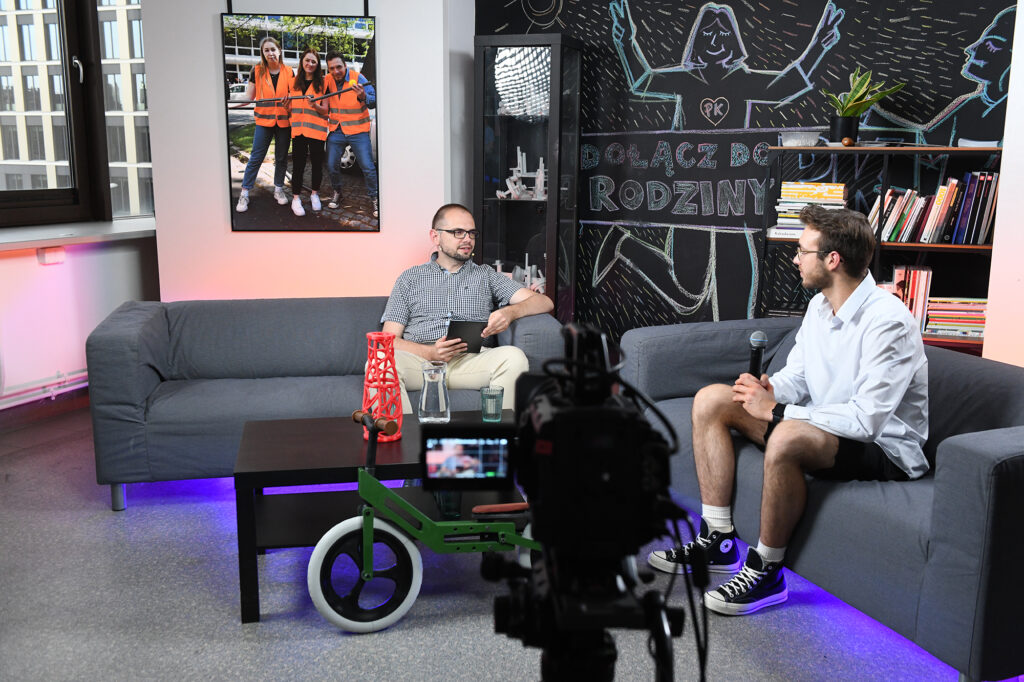 Studio nagraniowe. Na dwóch szarych kanapach siedzą: z lewej Bartłomiej Krystyński, z prawej - widoczny z profilu - Oskar Jurek. 