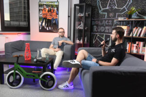 Studio nagraniowe. Na dwóch szarych kanapach siedzą: z lewej Bartłomiej Krystyński, z prawej - widoczny z profilu - Krzysztof Pszczółka