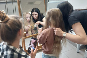 Najmłodsza uczestniczka akcji - Marysia stoi przed lustrem, a fryzjerka przygotowuje jej włosy do obcięcia