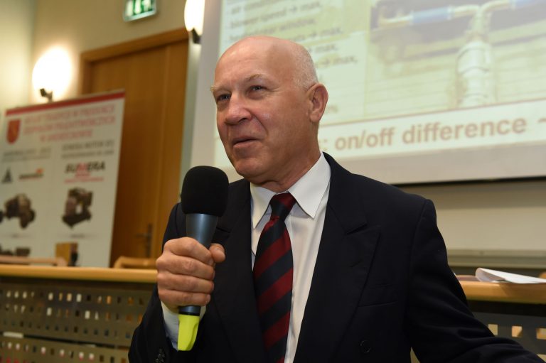Profesor Marek Brzeżański podczas wystąpienia. Trzyma w ręce mikrofon. Ubrany elegancko: marynarka, biała koszula, krawat. 