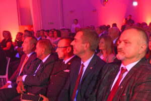 Spowita czerwonym światłem widownia. Pośród innych osób siedzi rektor Andrzej Szarata