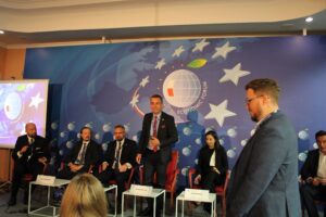 Rektor PK wśród współuczestników dyskusji. Stoi i uśmiecha się. Pozostali paneliści siedzą w fotelach