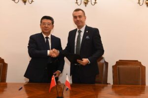 prof. Bai Haili i prof. Andrzej Szarata podają sobie ręce po podpisaniu umowy, na stole przed nimi flagi Chin i Polski