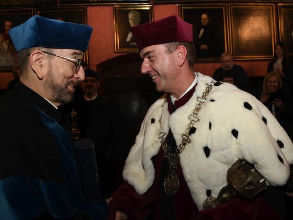 Rektor Andrzej Szarata w czerwonej todze z gronostajowym kołnierzem ściska dłoń mężczyźnie w czarno-niebieskiej torze i z brodą w okularach. Ten mężczyzna to profesor Bonenberg