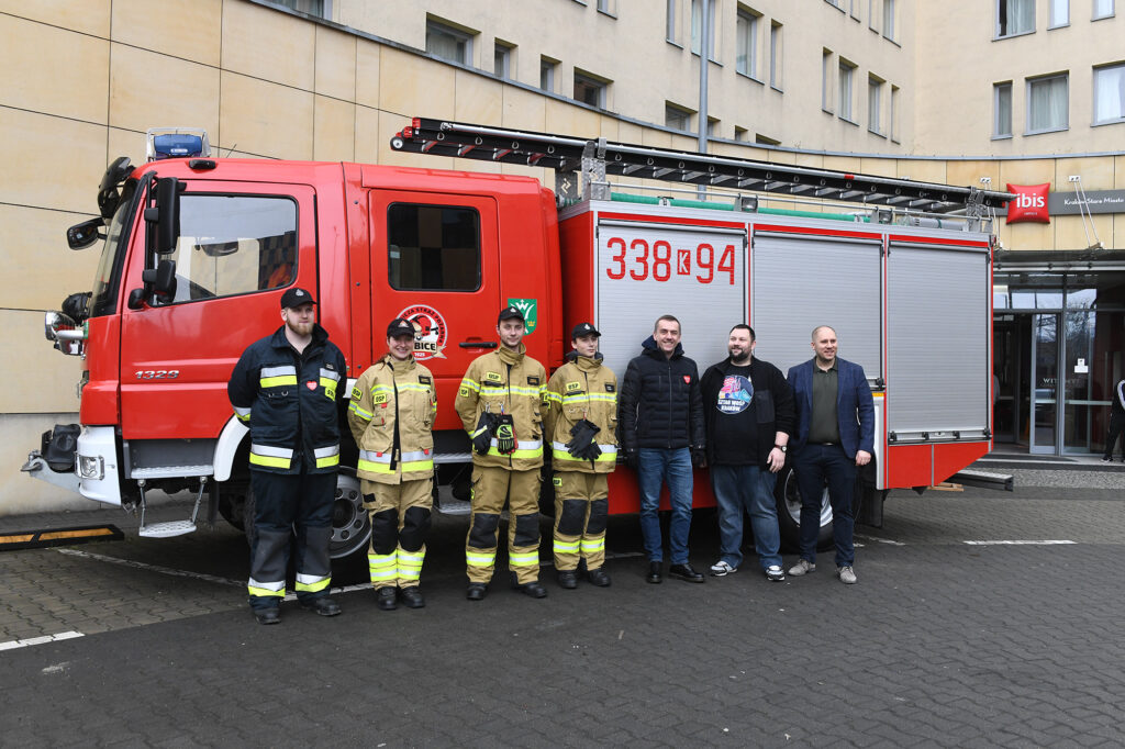Rektor pozuje do zdjęcia ze strażaczkami i strażakami na tle wozu