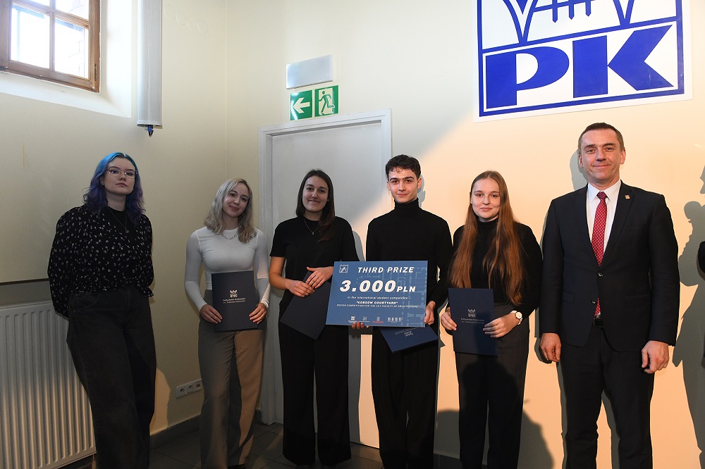 Zdobywcy III nagrody pozują do wspólnego zdjęcia z rektorem PK. Student w środku trzyma symboliczny czek na 3 tys. zł