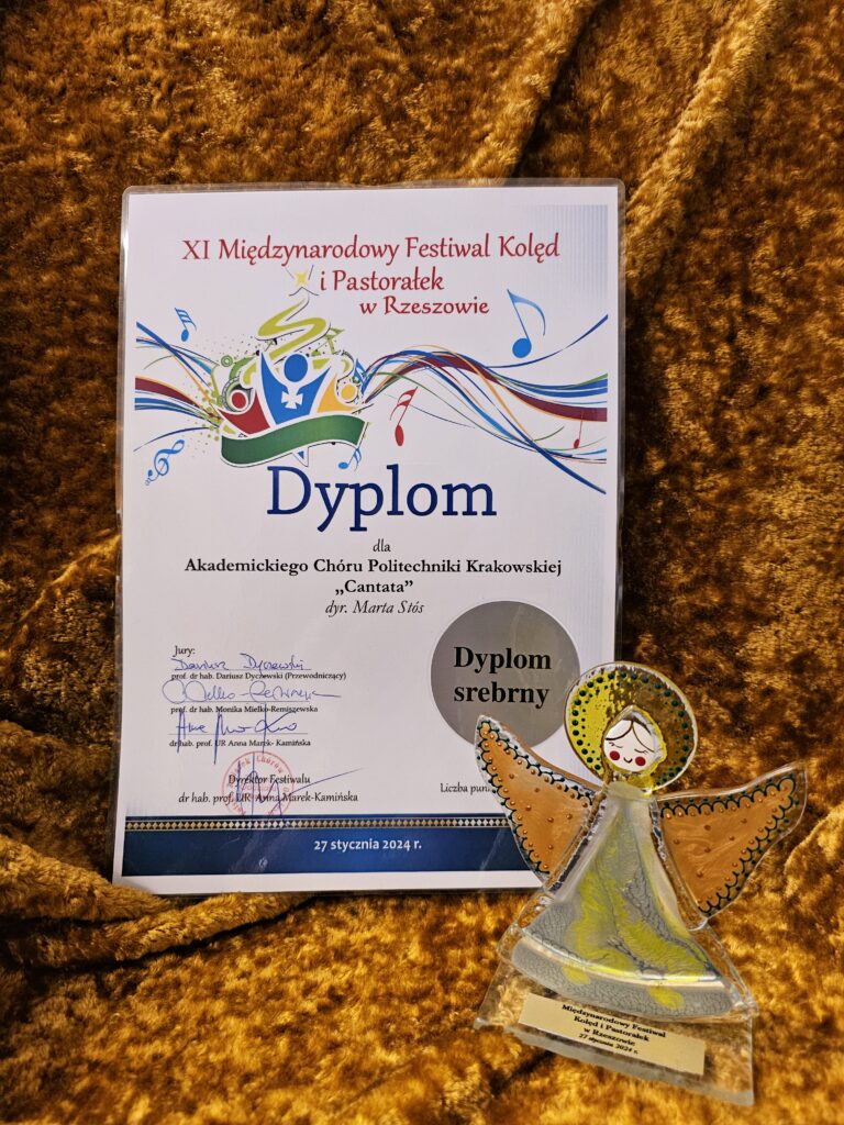 Na górze dyplomu nazwa i grafika wydarzenia. Na środku informacja dla kogo jest prznaczony. Pod spodem podpisy jury. Obok dyplomu stoi statuetka w kształcie anioła.