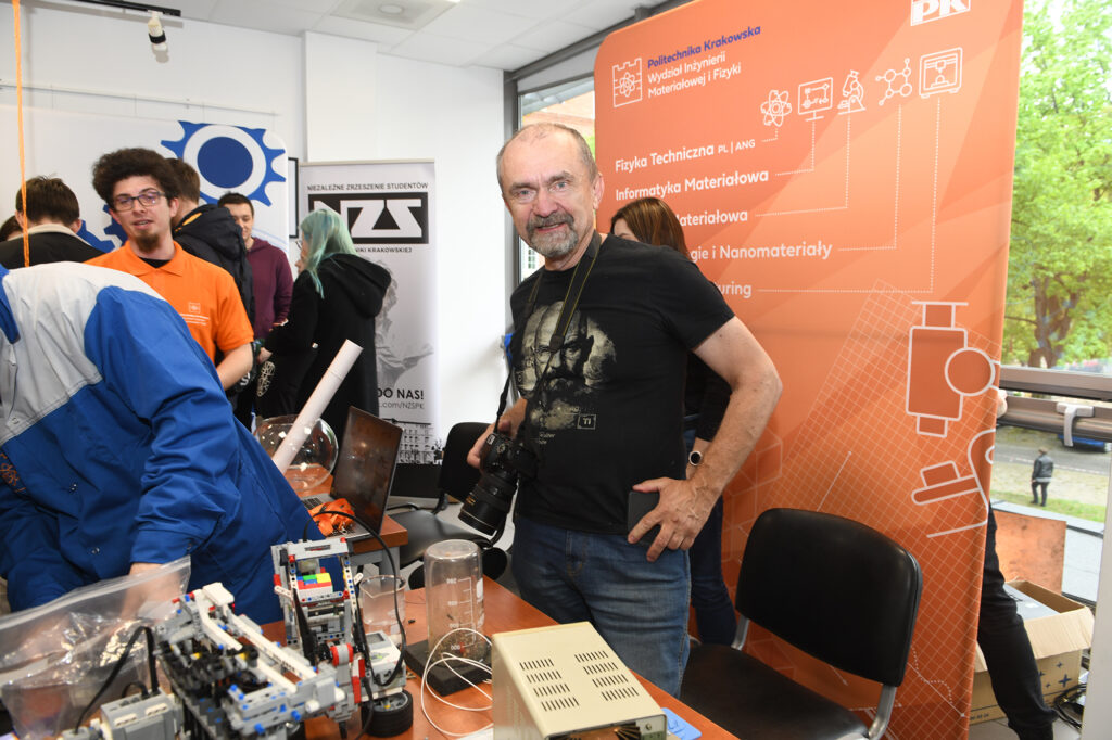 Starszy mężczyzna uśmiecha się do zdjęcia. Na stoliku przed nim leżą różne techniczne urządzenia