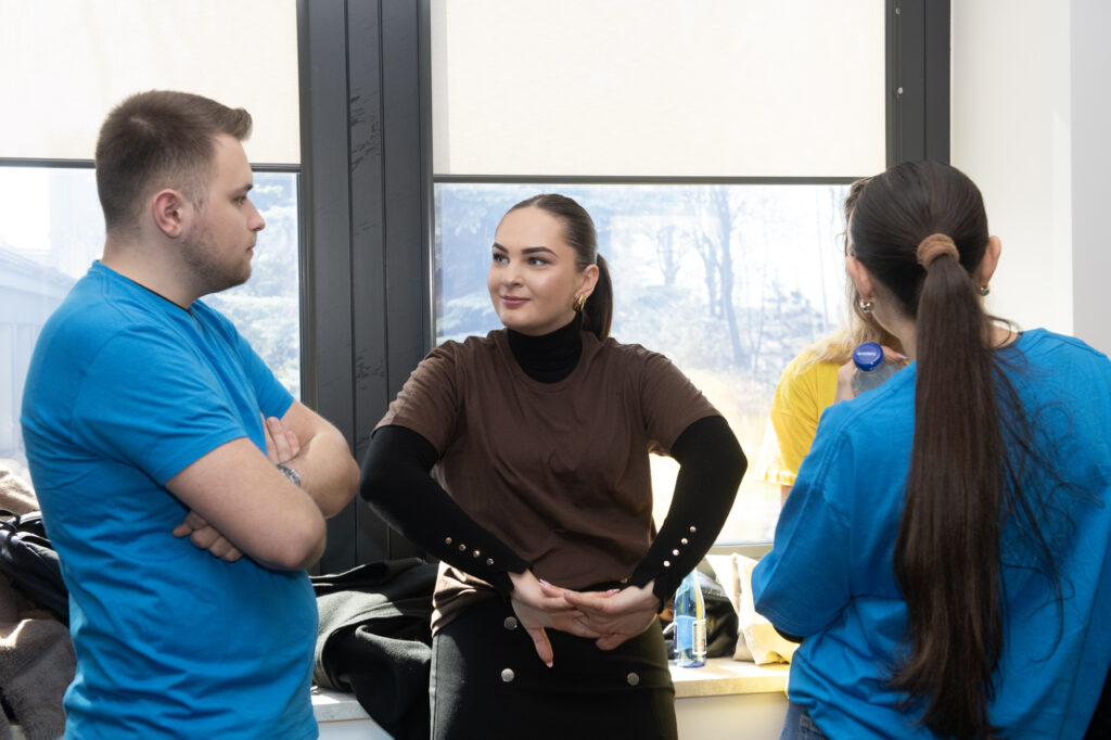 Troje studentów, dwie dziewczyny i chłopak dyskutują. Jedna dziewczyna na brązową koszulkę, pozostali - niebieskie