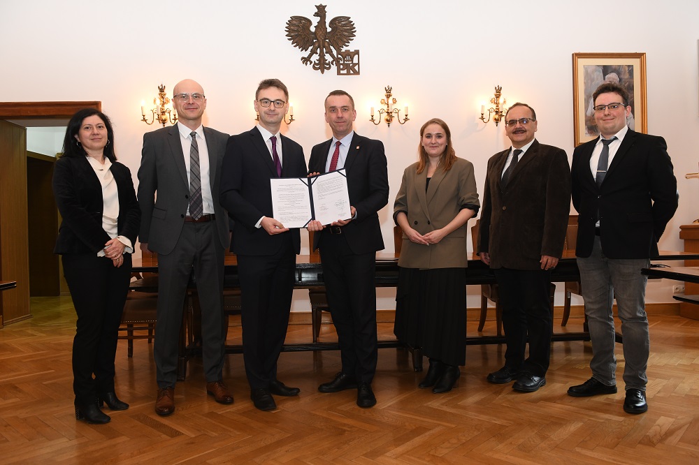 Uczestnicy spotkania pozują do zdjęcia. Prof. Andrzej Szarata i Marcin Karp trzymają egzemplarz umowy