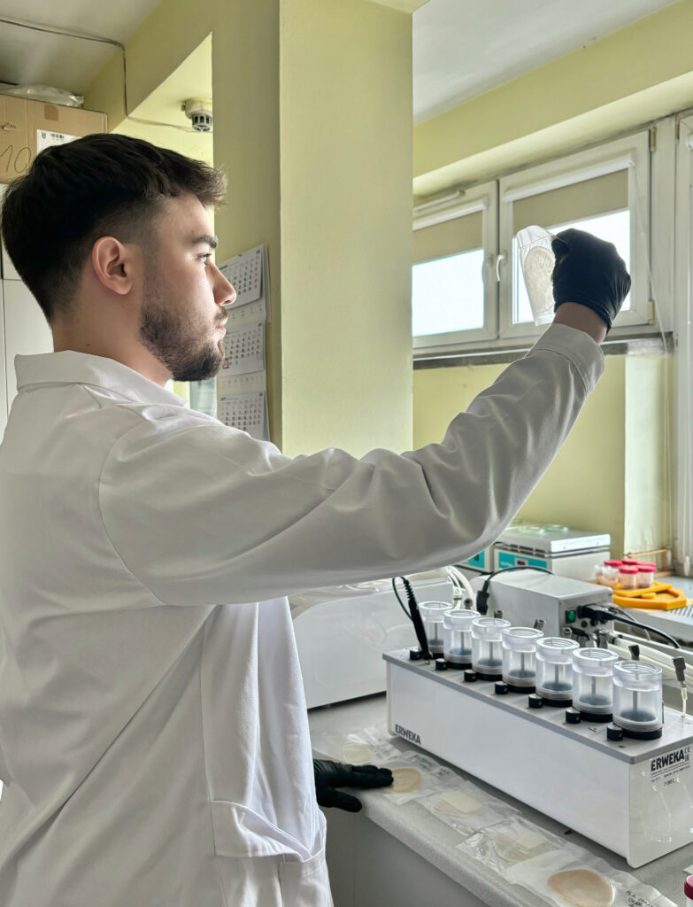 Kacper Odziomek podczas pracy w laboratorium. Ma na sobie kitel chemika, na stole probówki