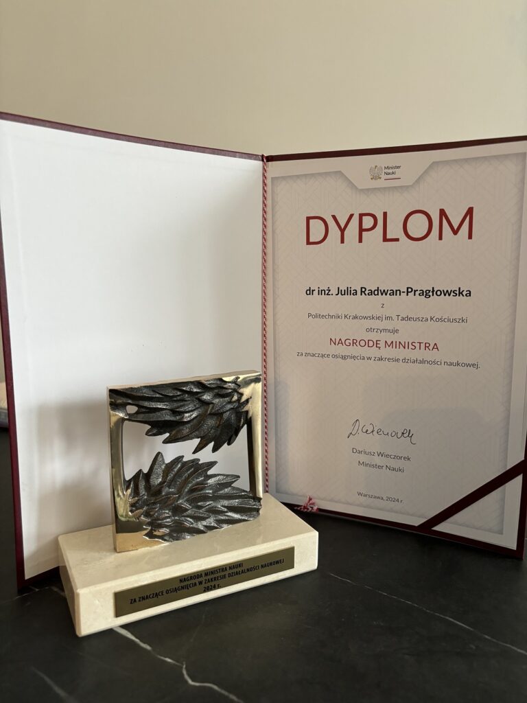 Nagroda Ministra Nauki - statuetka przedstawiająca jakby dwa liście, w tle dyplom dla Julii Radwan-Pragłowskiej. W dyplomie krótka informacja o rodzaju i kategorii nagrody