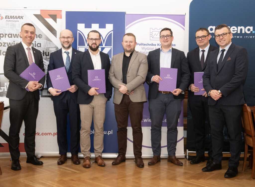 Grupa siedmiu mężczyzn pozuje do wspólnego zdjęcia. Sześciu z nich trzyma fioletowe teczki.