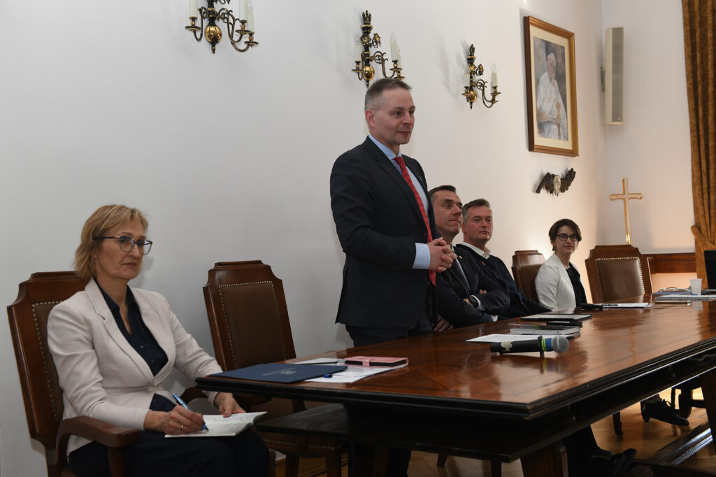 Za stołem prezydialnym stoi i przemawia prorektor Marek Bauer, pozostali uczestnicy siedzą